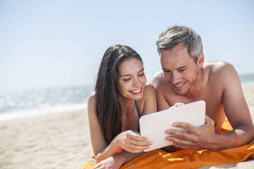 handsome couple on the seaside lying on a beach towel to use a digital tablet